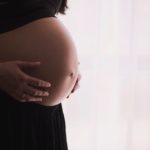 woman's with her hands on her exposed pregnant belly